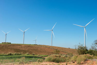 Windmills on hill against clear blue sky