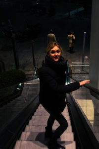 High angle portrait of young woman standing on escalator at night