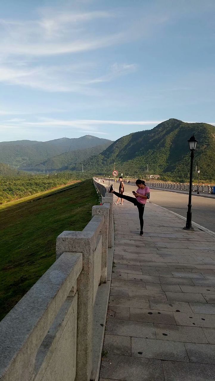 real people, sky, one person, full length, leisure activity, lifestyles, nature, mountain, beauty in nature, day, scenics - nature, environment, women, casual clothing, sunlight, men, non-urban scene, adult, rear view, outdoors, mountain range