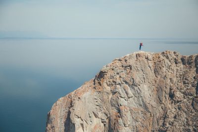 Rear view of man on cliff by sea against clear sky