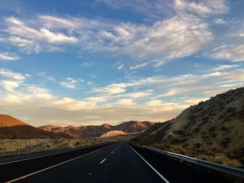 Empty road leading towards mountains against sky