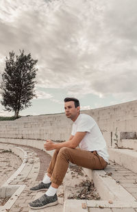 Side view of young man sitting against sky