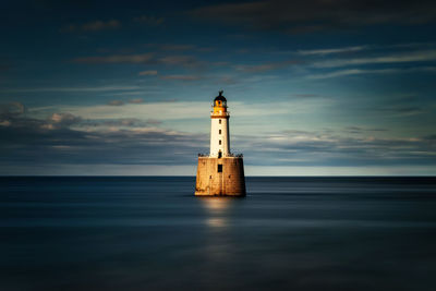 Lighthouse by sea against sky during sunset