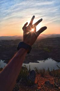 Sunbeam through hand against sky during sunset