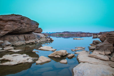 Rocks by sea against clear blue sky