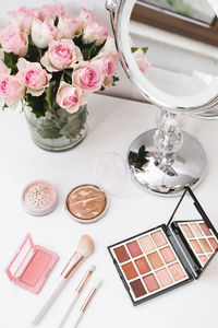 Cosmetics for make-up, round mirror and roses flowers on table. decorative cosmetics, brushes, eyes