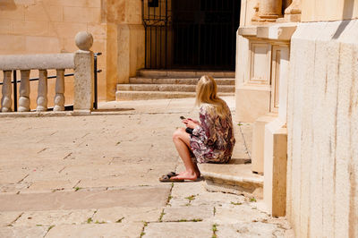 Woman sitting on staircase by building