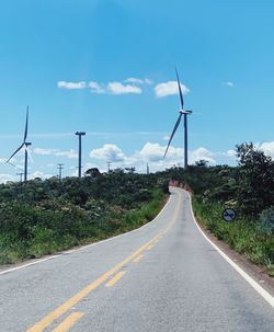 Road by wind turbines against sky