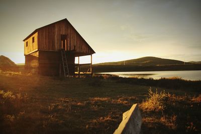 Built structure on land by lake against sky during sunset