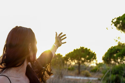 Woman with hand raised against clear sky