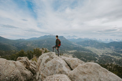 Man standing on rock looking at mountains against sky