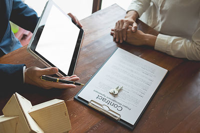 Cropped image of real estate agent showing digital tablet to customer at table