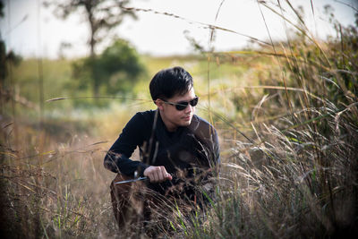 Young man kneeling by plants on field