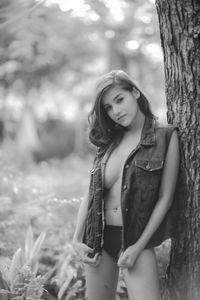 Portrait of seductive woman wearing jacket standing by tree trunk in forest