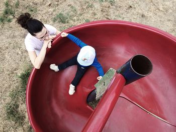 High angle view of mother looking at son playing on slide at playground