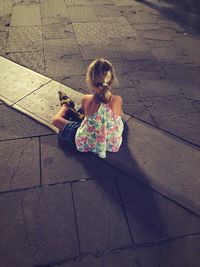 High angle view of girl sitting on footpath