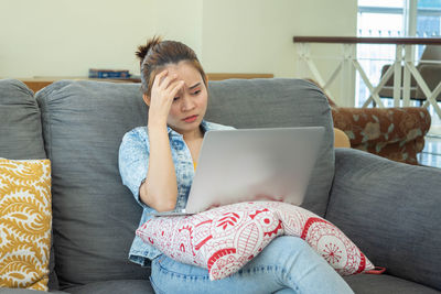 Young woman using mobile phone while sitting on sofa