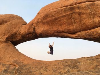 Man jumping on rock formation against clear sky