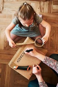 Woman writing an address on a cardboard box parcel in room at home. little girl helping her mother