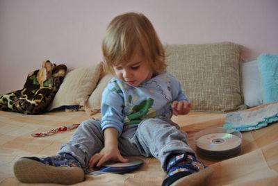 Cute boy playing with compact discs on bed at home