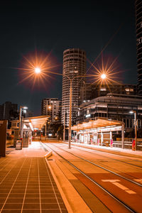 Light trails on road by buildings against sky at night