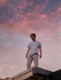 Low angle view of young woman standing on roof against sky