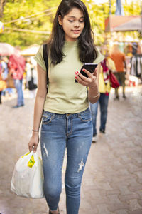 Full length of woman using mobile phone in city