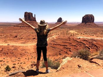 Woman with arms outstretched standing on dirt road against sky