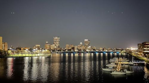 Illuminated buildings by river against sky at night