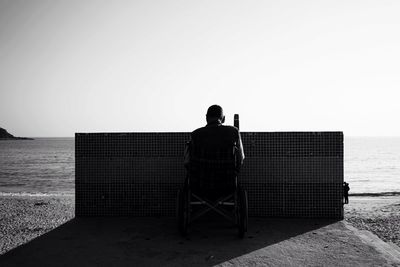 Rear view of disabled man on wheelchair at promenade against clear sky