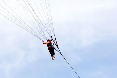 Low angle view of men hanging on rope against sky