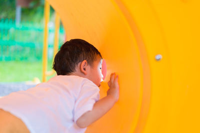 Cute boy looking through hole in yellow playground equipment