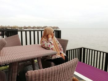 Woman sitting at outdoor cafe by sea against sky