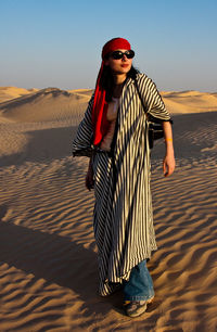 Young woman wearing sunglasses on sand in desert against sky