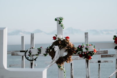 Close-up of flowers on cross by sea against sky
