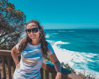 Portrait of smiling young woman standing at beach against clear blue sky