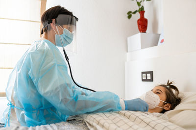 Doctor examining girl lying on bed at home