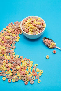 Healthy food concept, colorful ring cereal in bowl with spoon and arranged on light blue background.