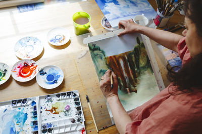 Woman with paintbrush doing watercolor painting at home