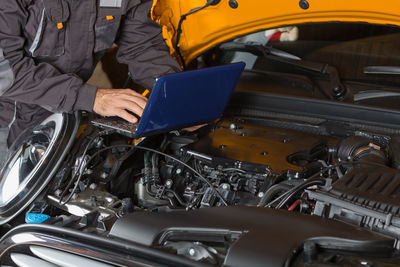 Midsection of mechanic using laptop on car engine at garage