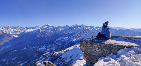 Man sitting on snowcapped mountain against sky