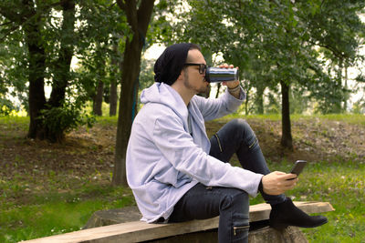 Rear view of man using mobile phone while sitting on tree