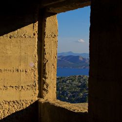 Old building by sea against sky seen through window