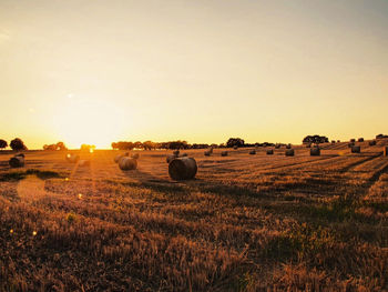 Hay bales on field against sky during sunset