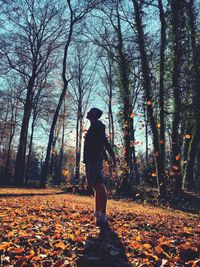 Man standing under falling leaves in forest during autumn 