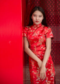 Portrait of beautiful young woman standing against red wall