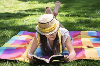 Full length of woman reading book while lying on picnic blanket in park