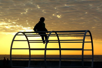 Rear view of silhouette man looking at sea against sky during sunset