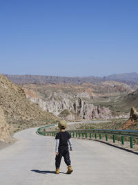 Rear view of woman walking on road against clear sky