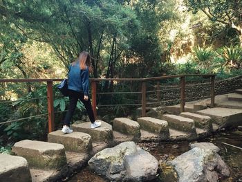 Rear view of woman walking on stones in forest